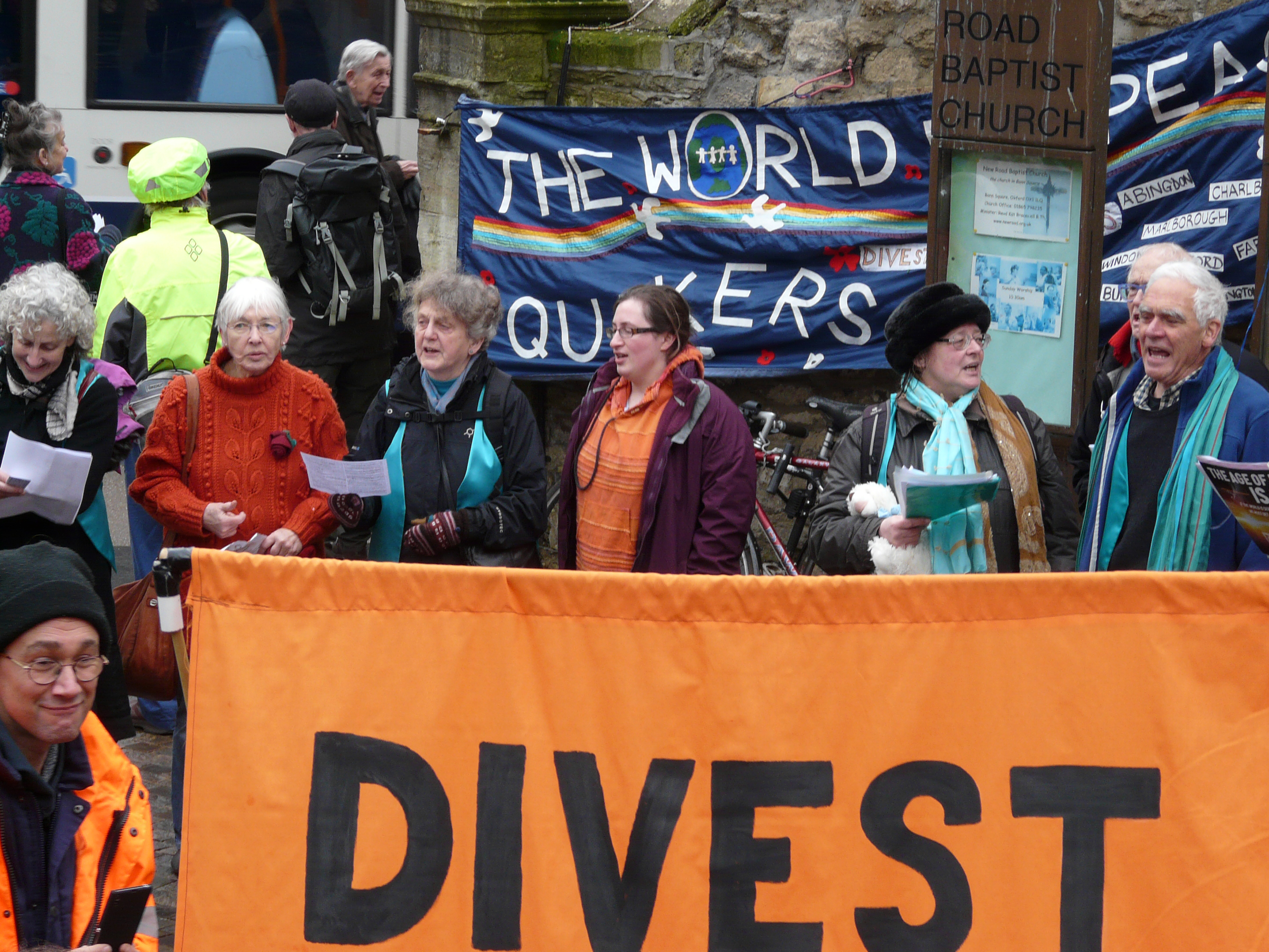  a dozen Quakers around huge organe banner saying Divest