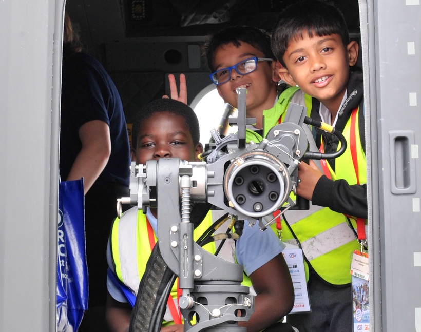 Several small boys grin as they crowd behind a machine gun pointing out of an aircraft