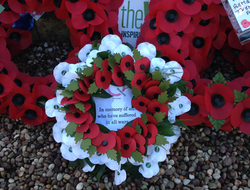 A wreath of red and white poppies stating "In memory of all who have suffered in all wars"