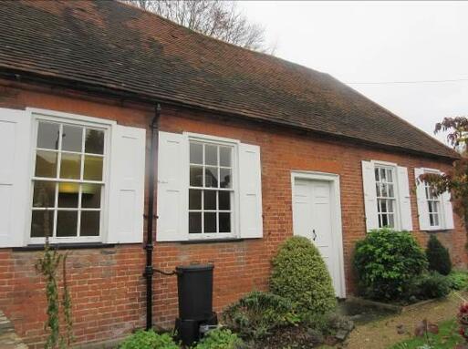 One storey brick house with four large windows flanked by white shutters. 