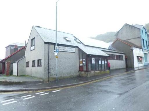 Grey building with solar panels on the roof faces onto a steep sloping road. 