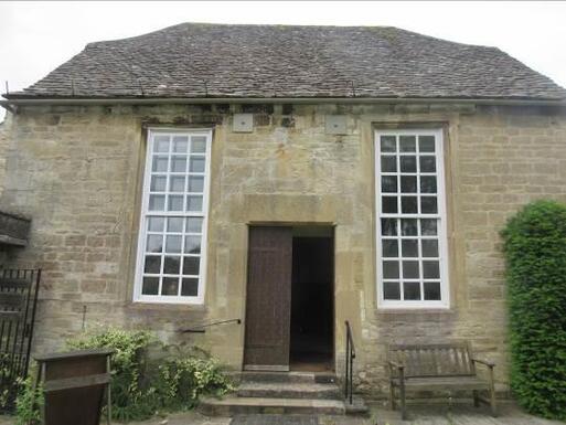 Short stone building with two long white windows flanking the central stone entrance steps and wooden front doors. 