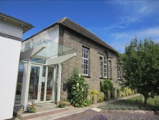 Stone building set in large gardens with glass-panel extension and extending canopy covering the entryway. 