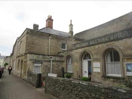 Seventeenth-century stone building with large arched windows and eroded 'Friends Meeting House' carving above entrance doors. 