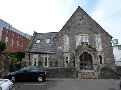 Distinct stone building with high roof gable and decorative detailing, set within a small car park.