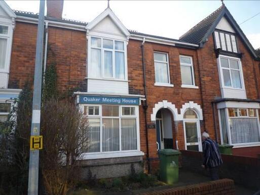 Terraced redbrick house with blue 'Quaker Meeting House' sign above front bay window.