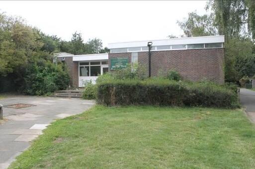 Flat roofed brick building with short steps leading to entrance, large lawn garden to front.