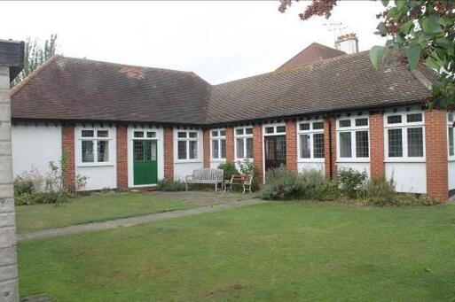 Single storey Alms-house style brick building within gardens. 