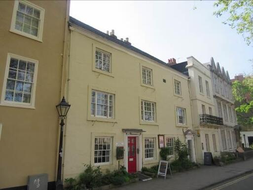 Yellow frontage of the building with red door with charming back garden.