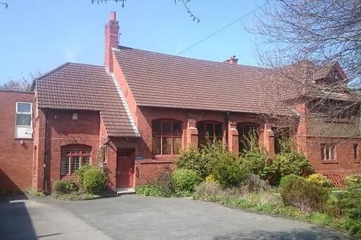 Large Victorian red-brick building with five large windows along its front. 