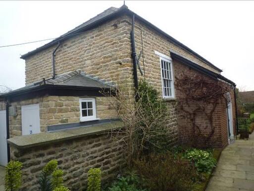 Small stone building with large windows and creeping plants growing up its entrance porch.