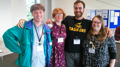 Four young adults, smiling, with their arms over each others' shoulders