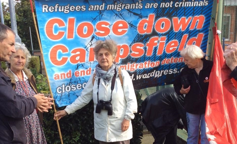 A group of protestors stand in front of a large blue banner which reads 'Close down Campsfield'