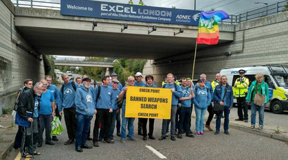 people in blue hoodies standing in a line holding a sign saying 'checkpoint: banned weapons search'