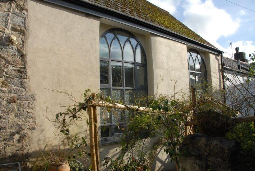 a single storey stone building with large windows is photographed from a neighbouring garden. 