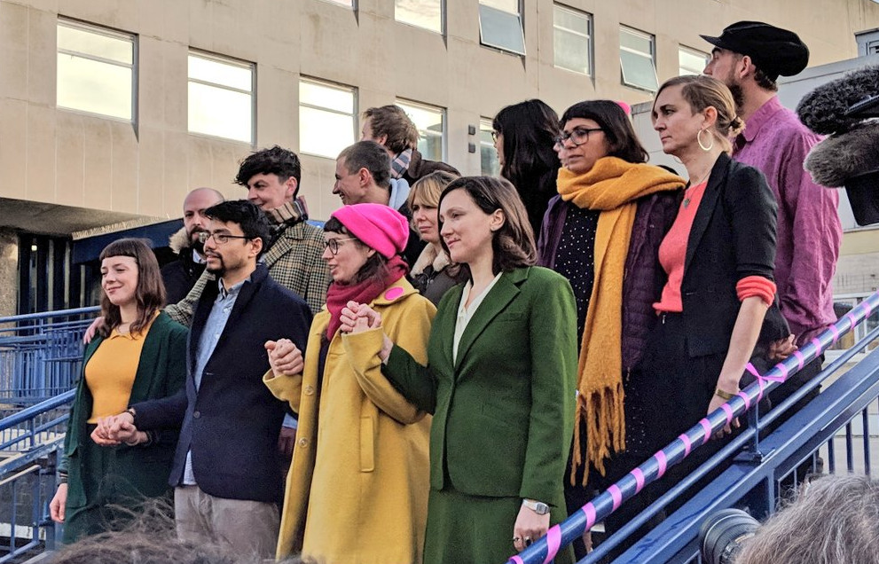 15 stand on court steps, pink scarves