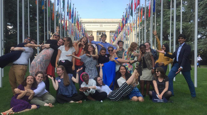 a group of young adults standing on a lawn with flags of different countries in the background and a building behind them titled 'United Nations | Nations Unies'