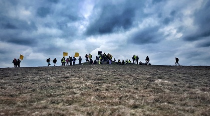 people gathering at the crest of a hill under a dramatic sky