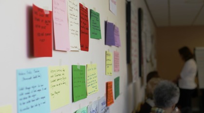 colourful cards with writing on them arranged neatly on a wall while people pay attention in the background