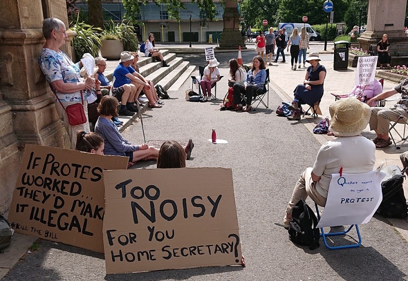 circle of dozen silent Quakers +banners on noise