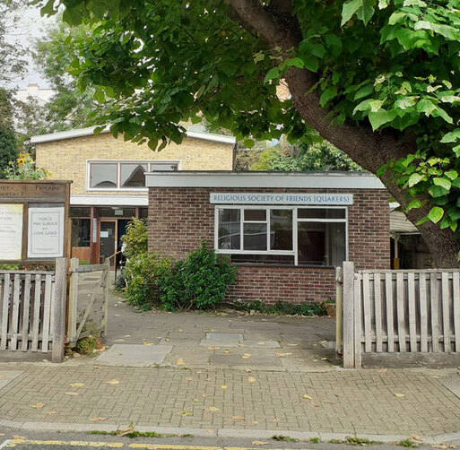 Split-level brick building behind large gate, a Quaker Meeting House sign tops the large square window.