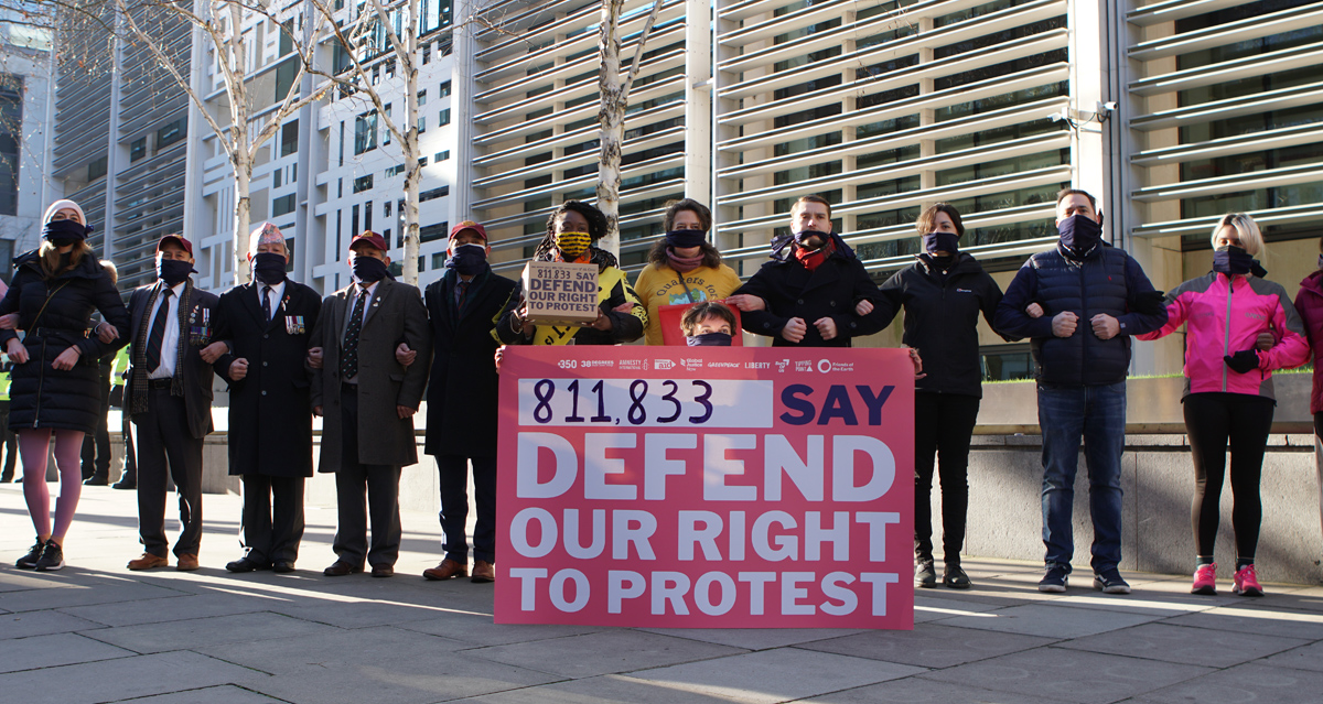 A group of people with linked arms gathering around a large placard which reads 811,833 say defend our right to protest