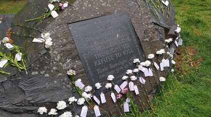 Wet conscientious objectors' memorial stone covered by white carnations. Plaque reads: to all those who have established and are maintaining the right to refuse to kill. Their foresight and courage give us hope.