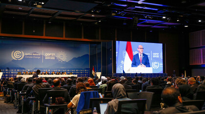 The COP27 plenary with delegates in chairs assigned to seating and Simon Stiell, UNFCCC executive secretary speakng at the podium and on a big screen. The COP27 logo can be seen on the stage background.