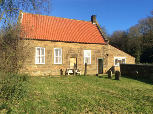 Simple house stone built with a red roof and burial grounds.