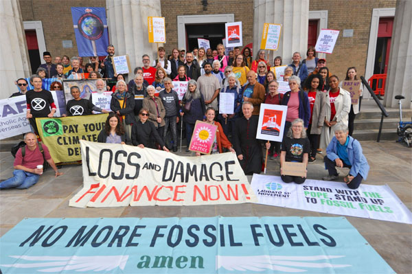 Faith groups gathered on the steps of a church with banners and placards asking for loss and damage finance.