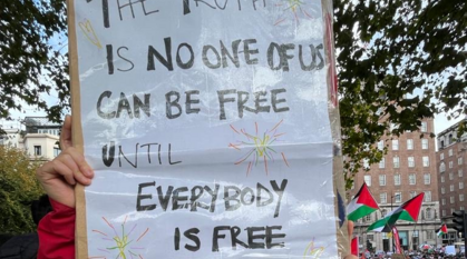 Person in a Quakers for climate justice t-shirt holding up a sign at a ceasefire rally with a quote from Maya Angelou "The truth is no one of us is free until everybody is free"