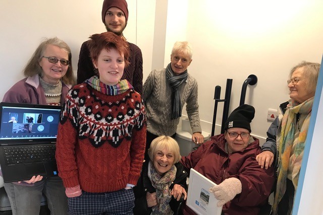 Group of Quakers, including one in a wheelchair gather together with some Friends on Zoom to celebrate