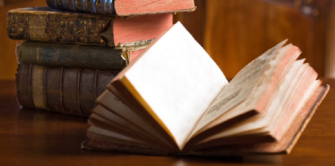 An antique book open in front of a pile of other antique books