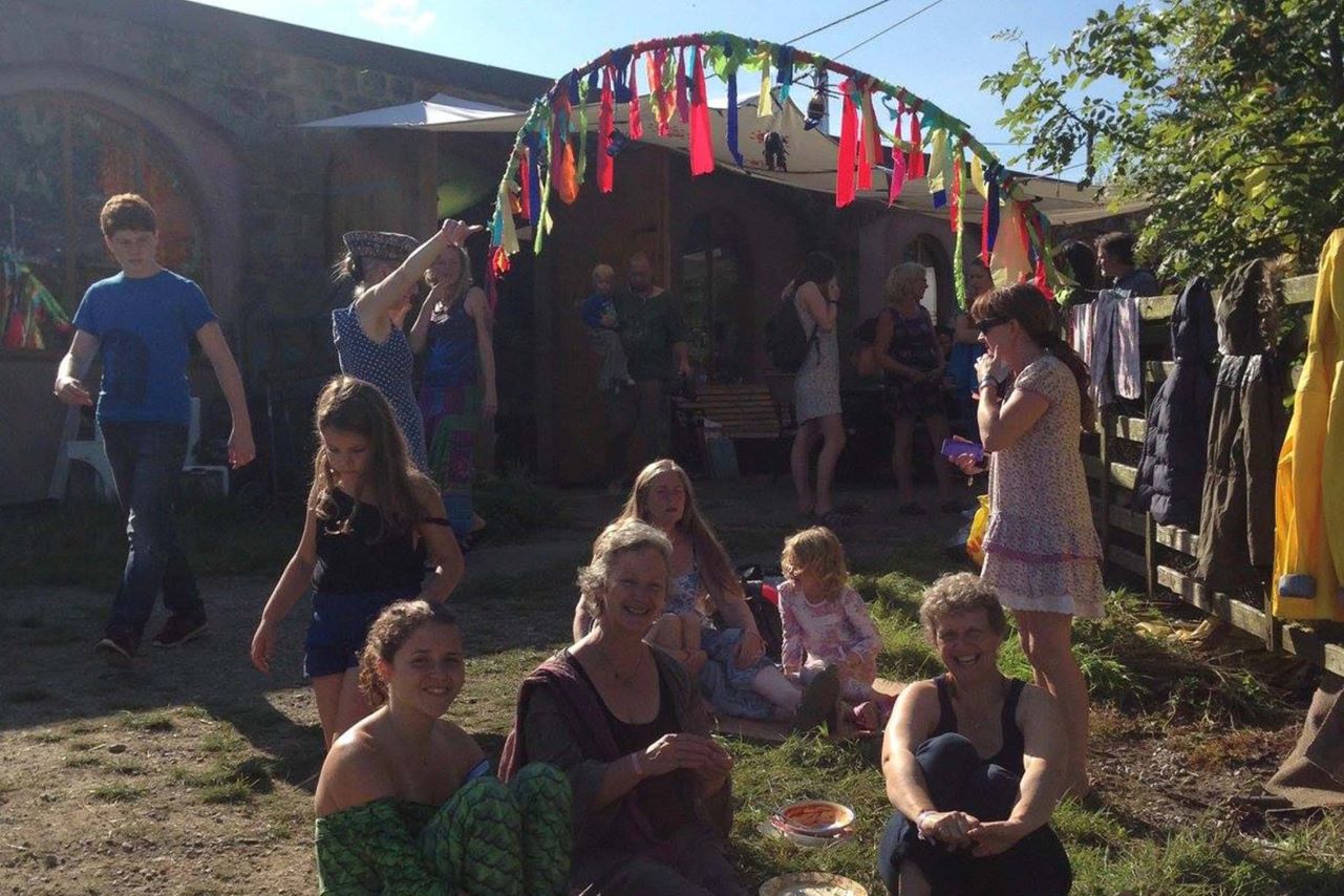 people sitting on a the grass, others holding up a ribbon arch and blue sky in background