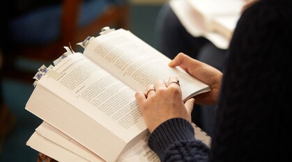 Close-up of a Friend's hands skimming through a heavily-tabbed copy of Quaker faith and practice, focusing on pages on the peace testimony