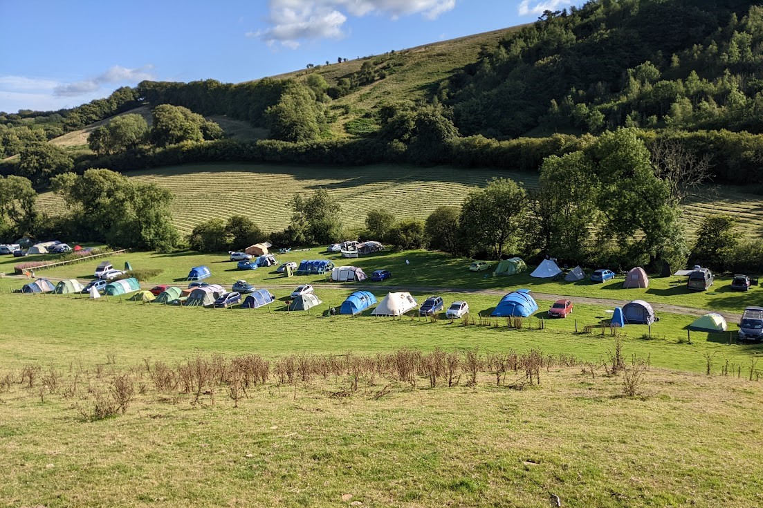 tents in a field in front of a grassy hill with blue skies in background