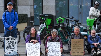 People sitting on the ground and standing in a Quaker meeting for worship at a 'Defend Our Juries' demonstration in central London. Their placards read: "The right of juries to give their verdict according to their conviction"