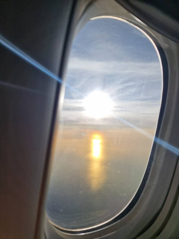 The sun sets outside the window of a plane