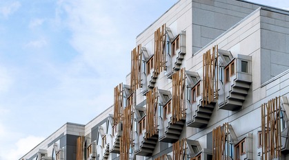 A focus on the distinctive windows of MSP offices in the Scottish Parliament building under a blue sky. The stone of the building with wooden panels and blue sky creates a serene palette.