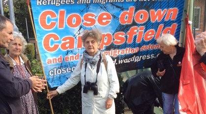 Bridget Walker holding up a lollipop sign that says "stop detention" outside an immigration detention facility