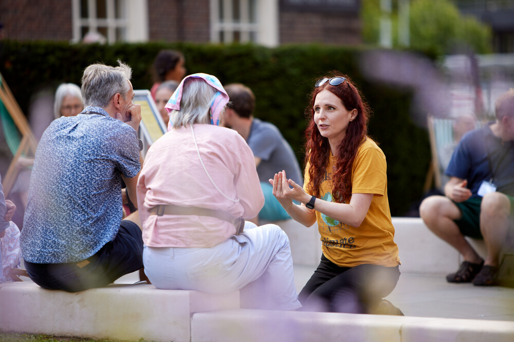 young adult in yellow tshirt crouching down talking to older people sitting down.