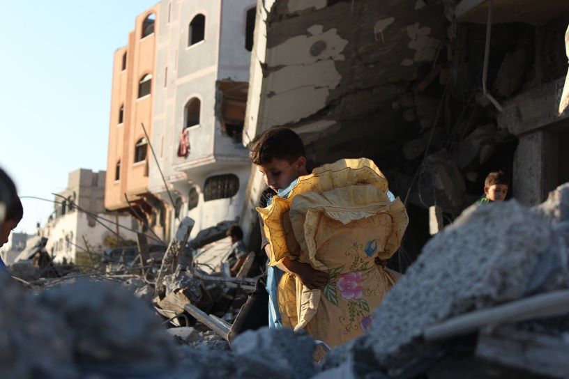 boy carrying pillows in rubble