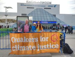 Two adults and a child standing by a banner outside the ExCel Centre in London. The banner reads 'Quakers for Climate Justice' 