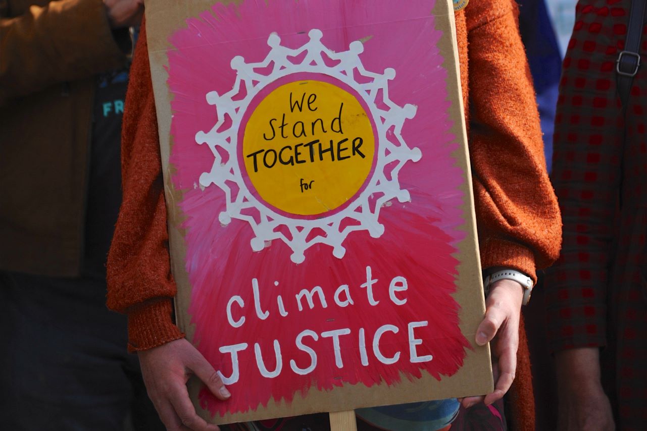 protestor holding colourful plaque saying 'We stand together for climate justice'