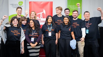 A group of people at a conference fringe event standing together wearing Make Polluters Pay T-shirts and cheering with fists in the air.