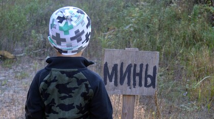 A child looks at a hand-painted sign that says "mines" in Ukrainian