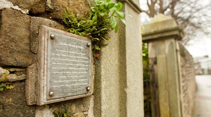 A stone wall outside a meeting house. The sign on the wall explains that a meeting house has been there for centuries