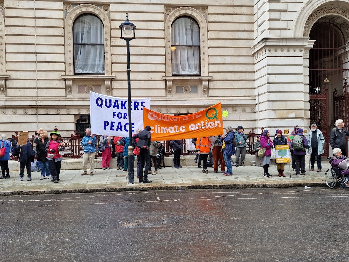 Quakers at an outdoor protest holding a bright orange banner reading 'Quakers for Climate Action' '