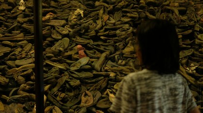 A person stands in front of a glass case of shoes taken from people interred and gassed at Auschwitz-Birkenau concentration camp.