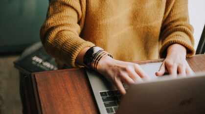 The torso of a person in a yellow jumper typing away on laptop